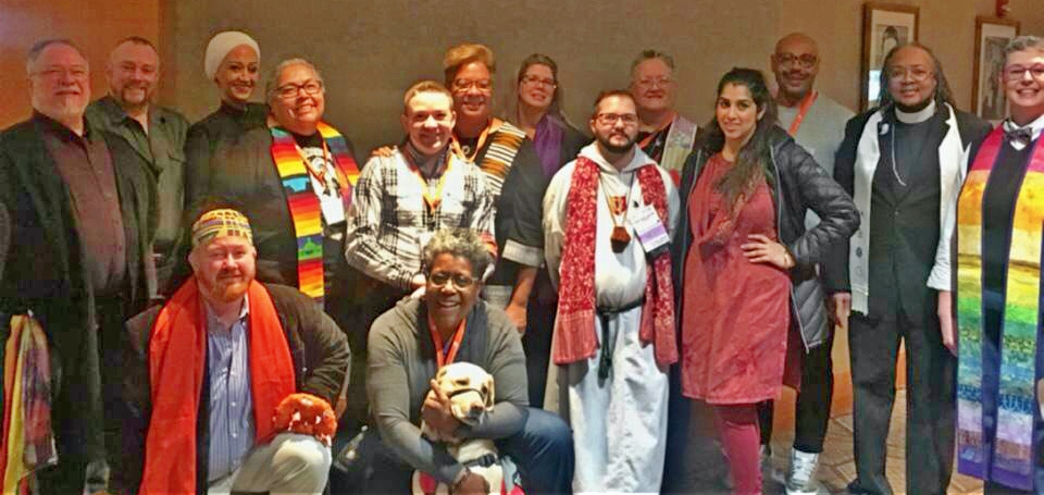 15 members of the 2018 spiritual care team, smiling; people of many ages, races, and religious/nonreligious dress, plus Sandy the chaplain dog